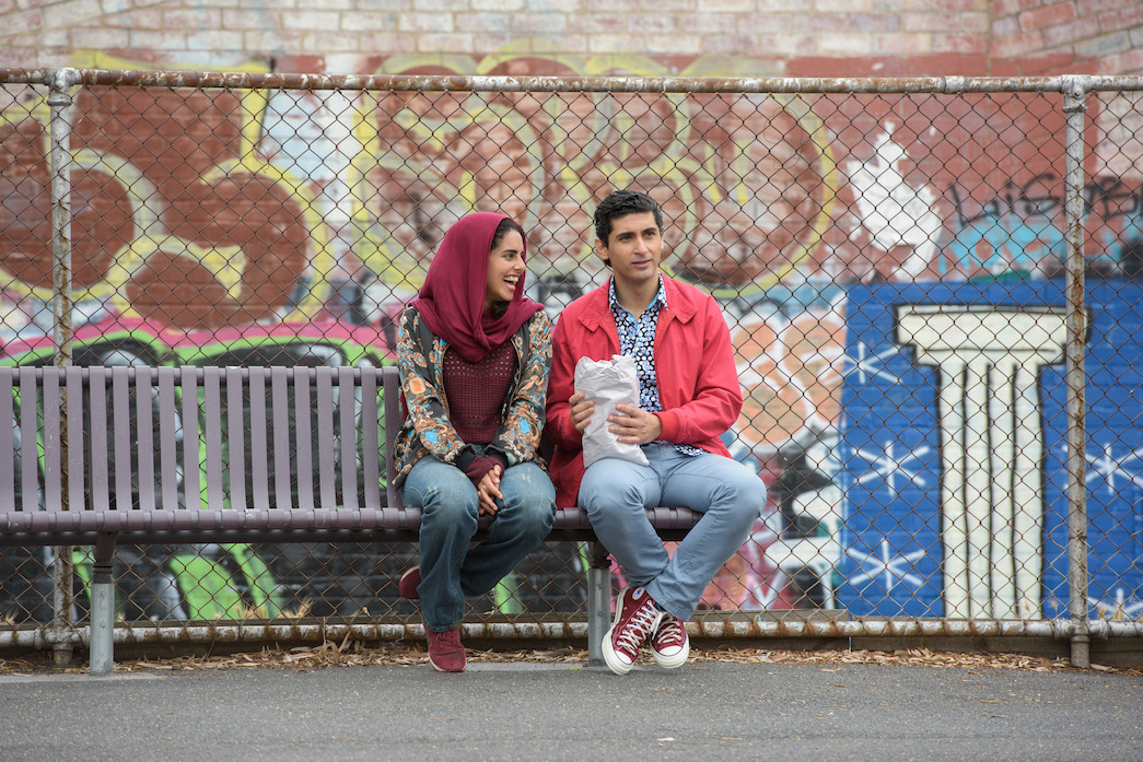 Osamah Sami in rolul lui Ali si Helana Sawires in rolul lui Dianne stau impreuna pe o banca in fata unui zid de graffiti in „Nunta lui Ali”.